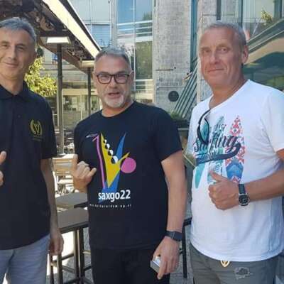 Three male musicians, energetically posing with thumbs up and flashing the 'Sign of the Horns' hand gesture.